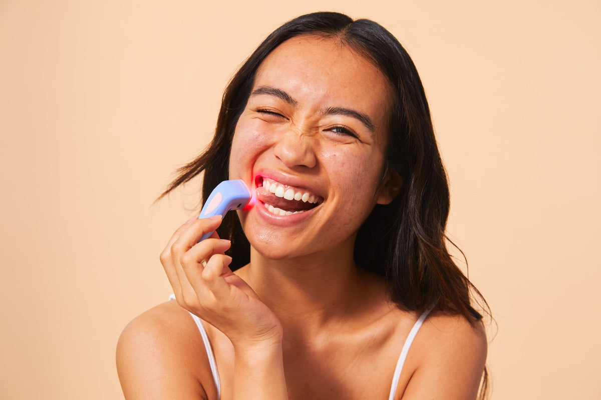 An image of a woman using a blue light therapy device for acne
