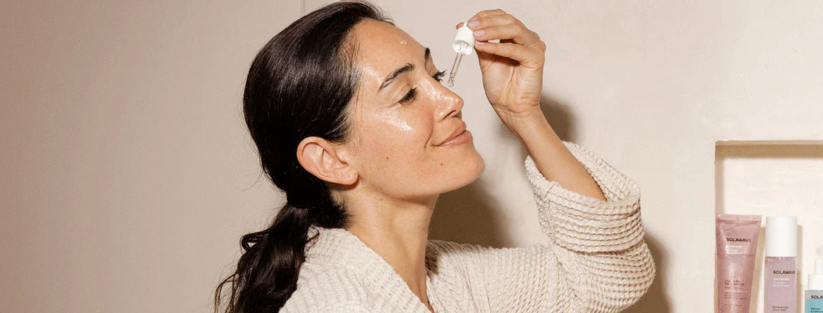 woman smiling while applying serum to face