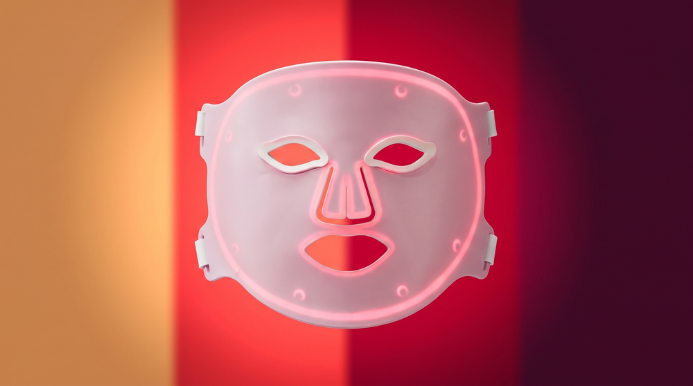 Solawave Wrinkle Retreat Pro LED face mask in front of four bands of coloured light representing its amber, red, deep red and near-infrared wavelengths.