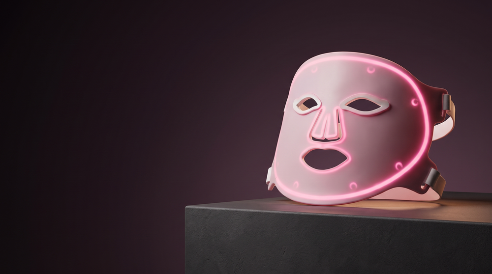 Solawave Wrinkle Retreat Pro LED face mask on a matte pedestal against a deep plum background with warm rim lighting.